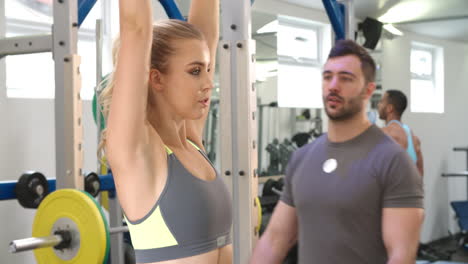 Entrenador-Asesorando-A-Una-Mujer-Haciendo-Ejercicio-Con-Pesas-En-Un-Gimnasio.