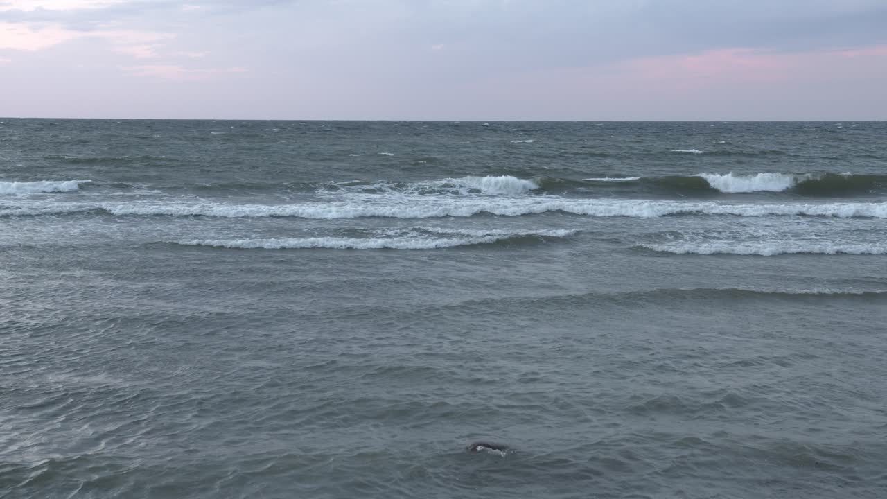 해가 지는 동안 발트해 해안에 부 ⁇ 히는 파도