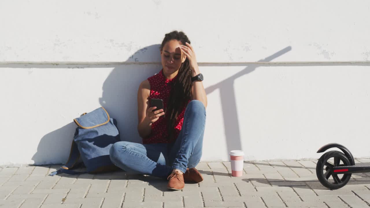 mujer afroamericana sentada y usando un teléfono inteligente en el paseo marítimo