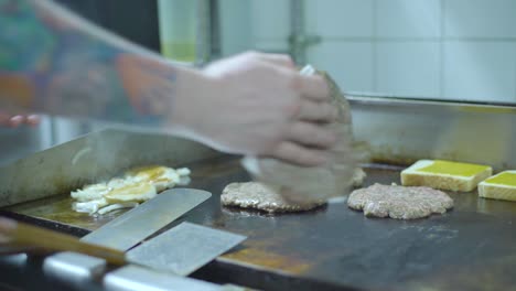 cooking in the back of a restaurant. deep fryer with fries and burger patties being placed and cooked.