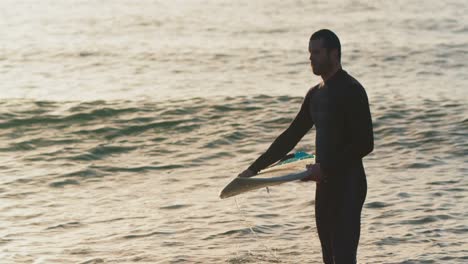 side view of mid-adult caucasian male surfer with surfboard standing in sea during sunset 4k