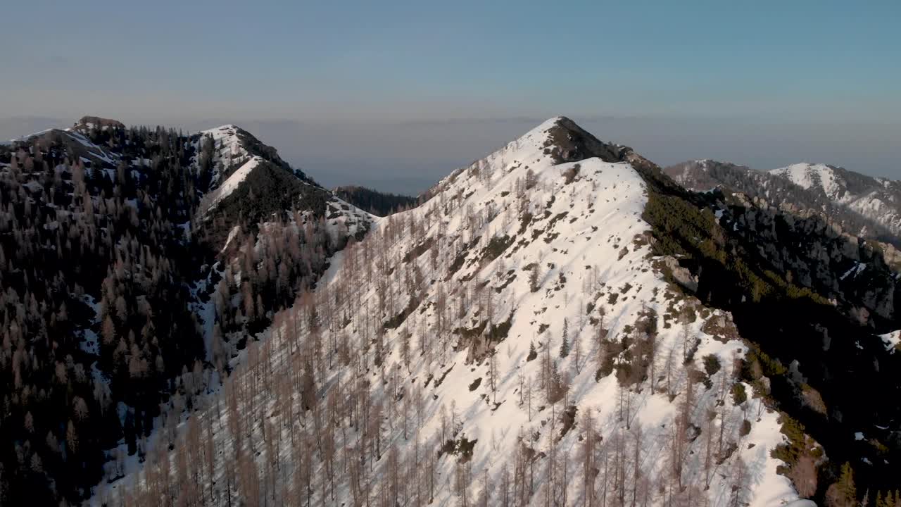 Drone flying straight following the ridge looking at the rest of the Karavanke alps in the background. Aerial view of the Karavanke Alps in the winter on a clear skies day