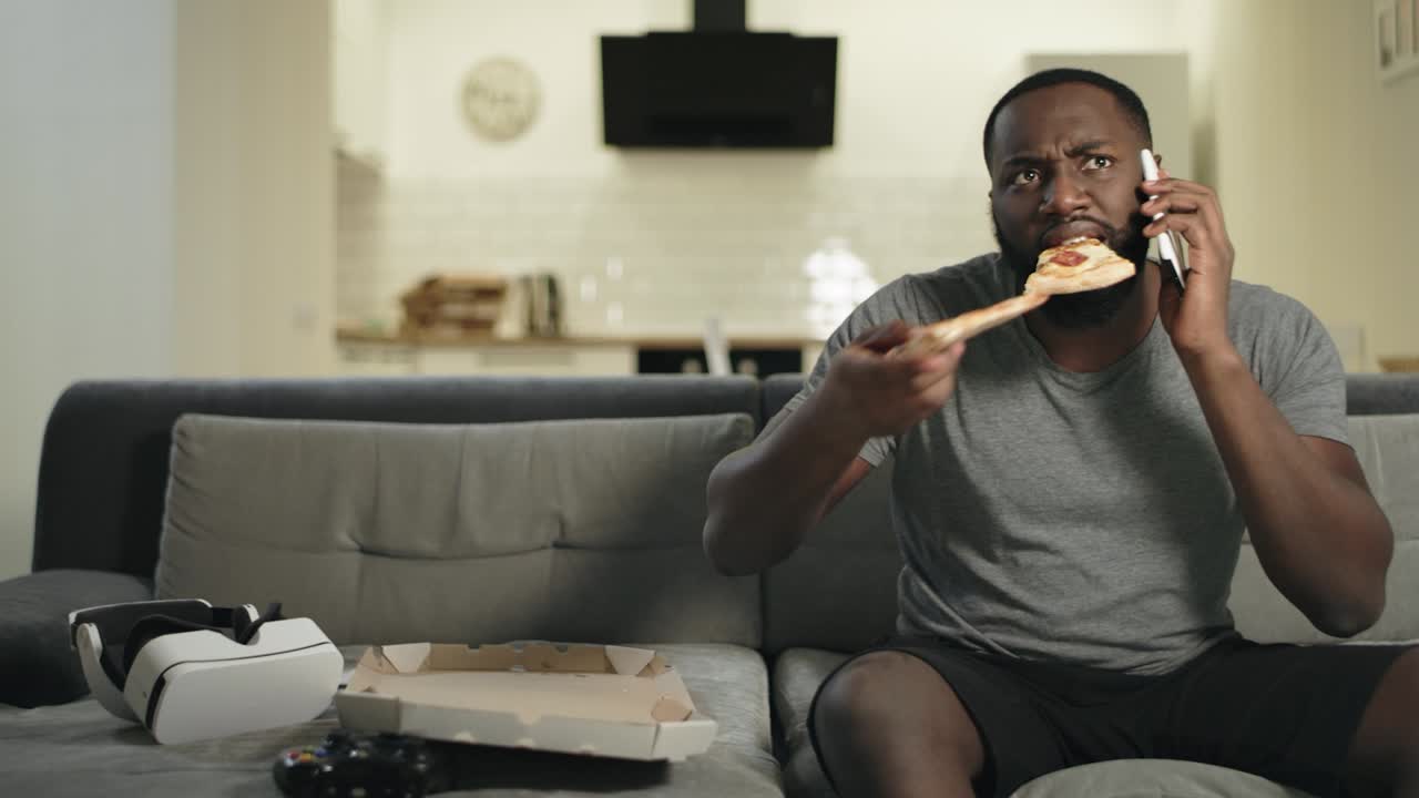 hombre concentrado hablando por teléfono con pizza. hombre negro viendo un partido de fútbol.