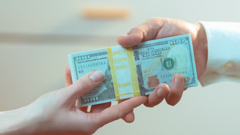 una mujer caucásica entregando a un hombre latino una pila de dinero