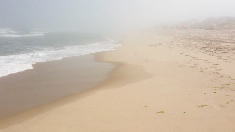 waves crash on the shore of a very foggy beach