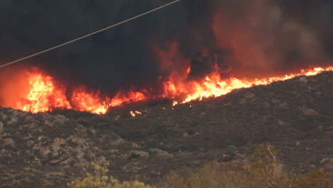 wild mountain fire with huge flame and fark smoke in the air