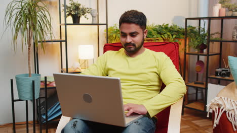 indian young man freelancer starts working on laptop sends messages makes online purchases at home