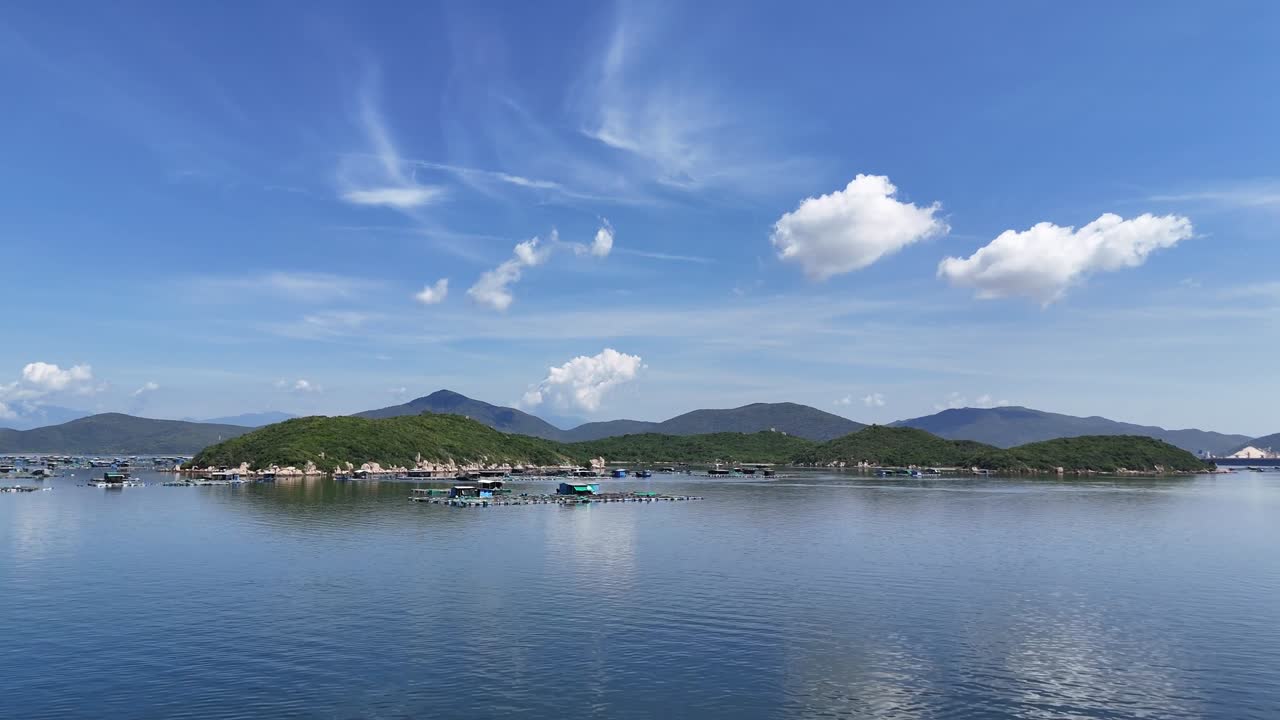 Scenic aerial footage of Cam Ranh Bay, Vietnam, showcasing serene waters, lush islands, and vibrant skies. Captures tranquil beauty with floating structures under bright, crisp daylight