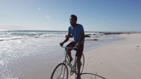 african american man smiling and riding bike on the beach