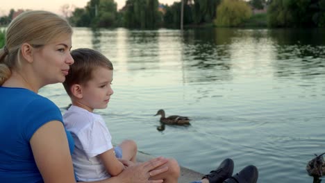 mother and child in medical masks feed ducks on the lake 03