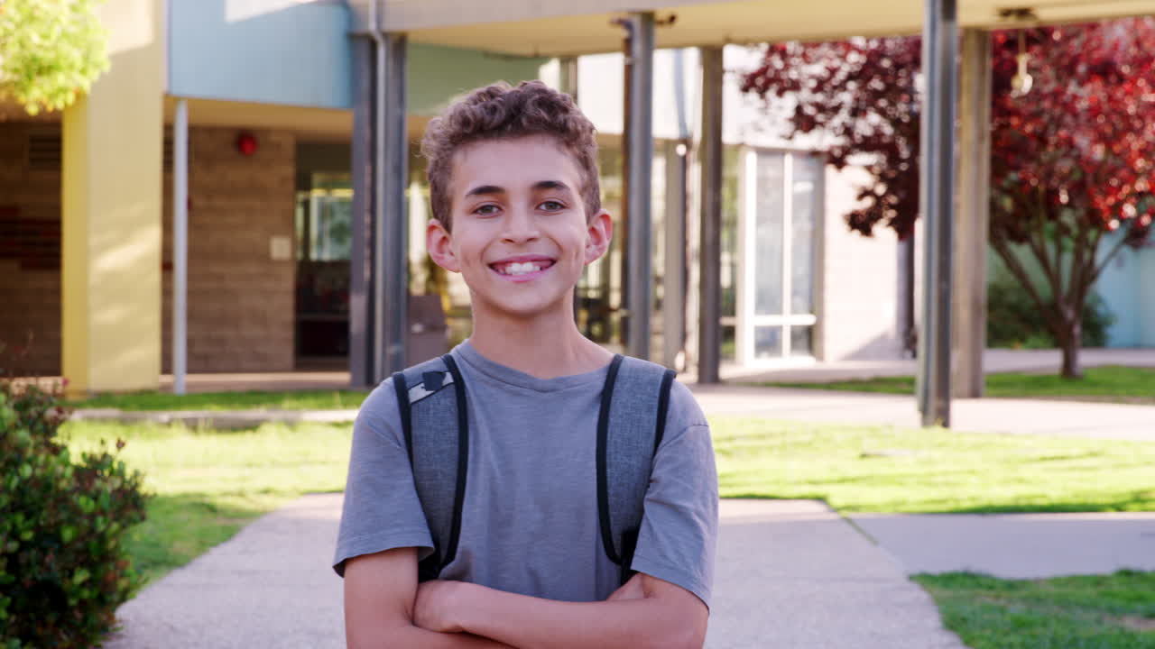 niño de escuela de raza mixta sonriente caminando hacia la cámara afuera
