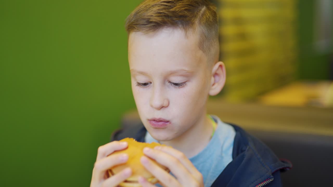 Young boy eating fries and burger sitting in cafe in city. Boy in a fast food cafe. Harmful nutrition