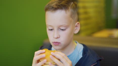young boy eating fries and burger sitting in cafe in city. boy in a fast food cafe. harmful nutrition