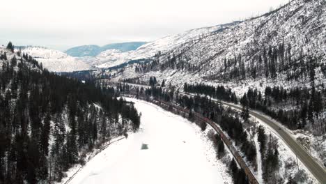 Tren-De-Carga-Viaja-A-Través-De-Un-Paraíso-Invernal-Congelado-En-Columbia-Británica:-La-Toma-Aérea-Sigue-El-Viaje-A-Lo-Largo-Del-Río-North-Thompson-Y-La-Autopista-5-De-Cabeza-Amarilla