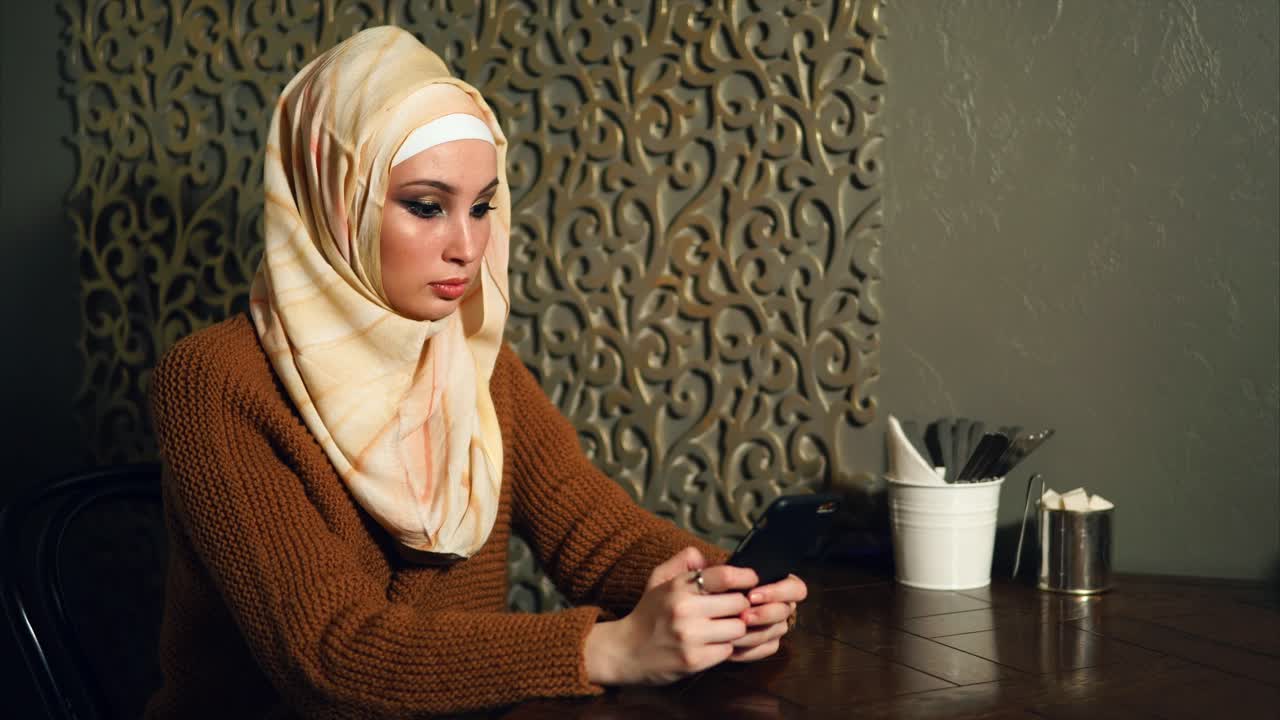 Woman using phone in a cafe wearing a hijab