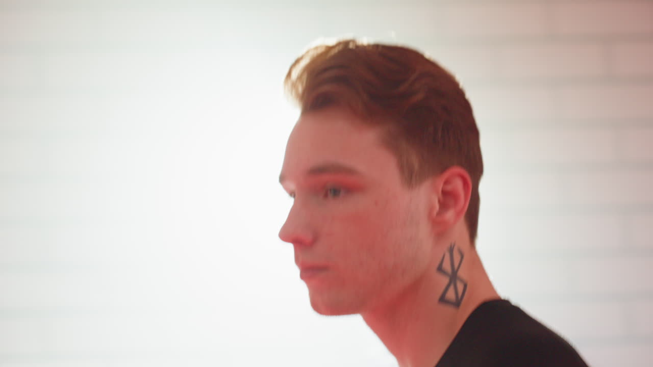 Side view of chap with short hair and neck tattoo jogging against brick wall, wearing black shirt, calm focused expression, representing individuality, strength, personality, and modern urban lifestyle