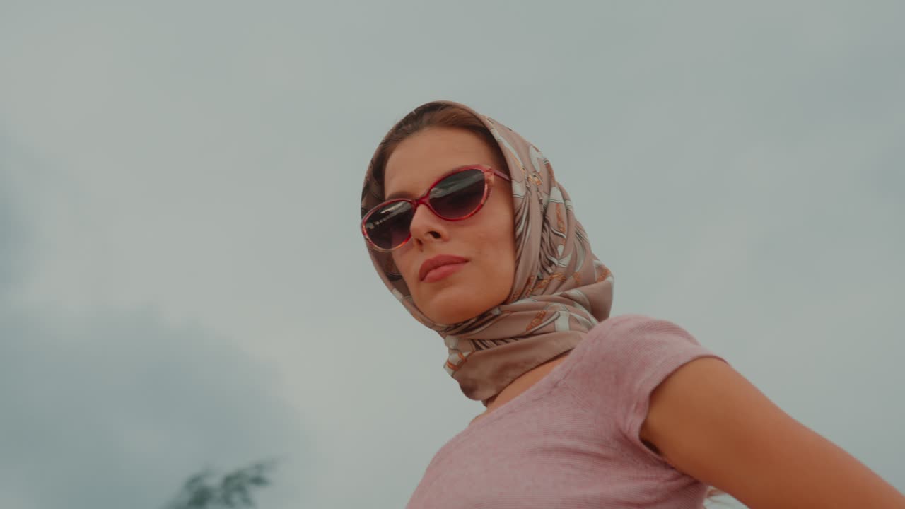A confident woman wearing a headscarf and sunglasses looks directly at the camera