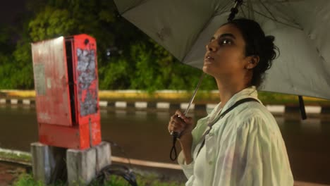 woman holding an umbrella on a rainy night waiting by the roadside