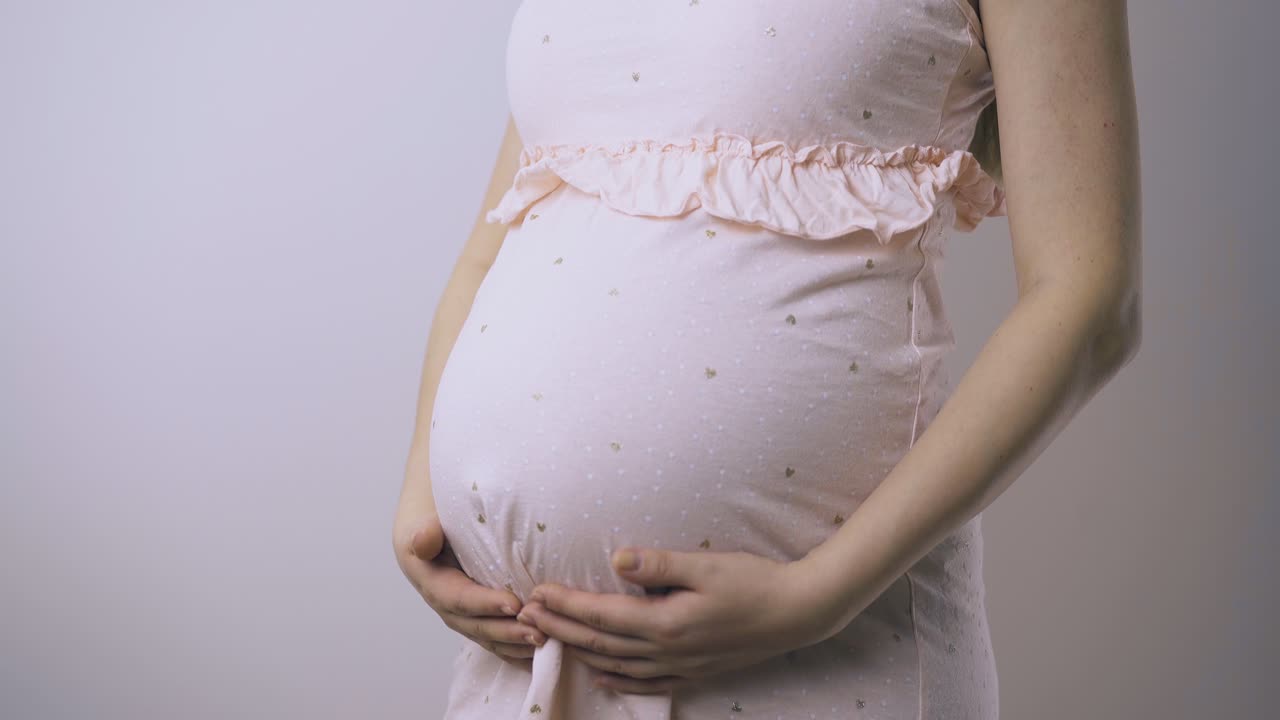 드레스를 입은 임신한 여성이 벽 클로즈업에서 아기  ⁇ 을 만집니다.