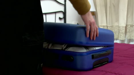 person packing a blue suitcase in a bedroom