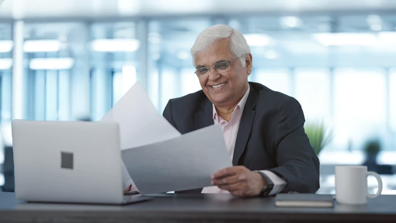 Feliz gerente sênior indiano lendo relatórios de negócios