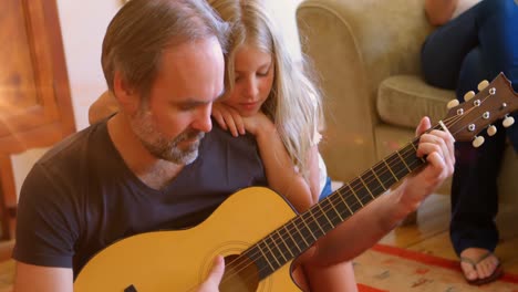 un padre y su hija tocan la guitarra juntos en su sala de estar en casa