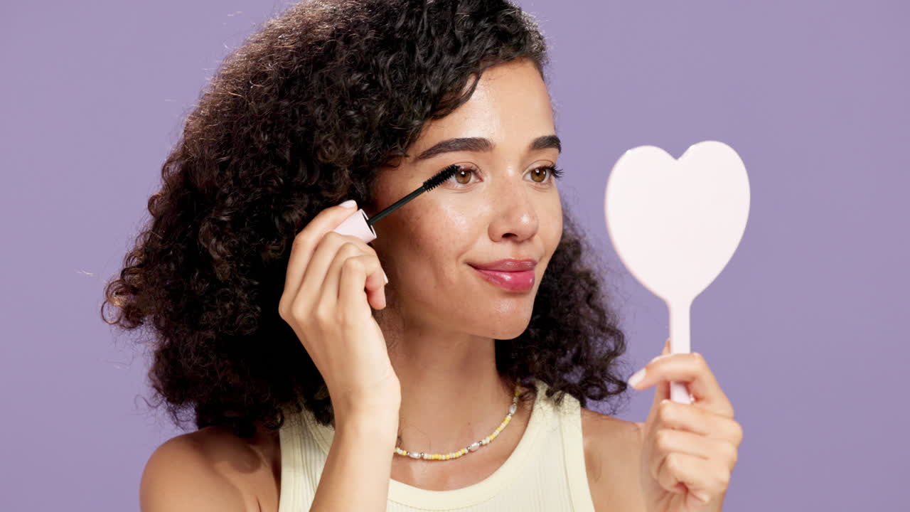 Woman applying mascara while looking in a heart-shaped mirror