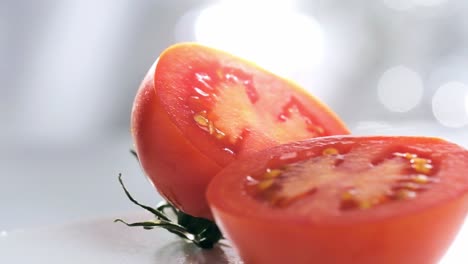 Toma-En-Cámara-Lenta-De-Dos-Mitades-De-Tomate-Girando-Sobre-Fondo-Blanco-Borroso,-Primer-Plano