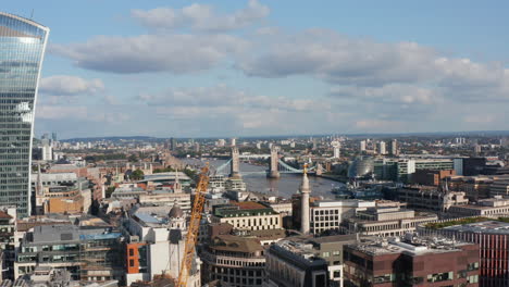 Aerial-view-of-buildings-around-River-Thames-at-Tower-Bridge.-Sliding-reveal-of-tall-futuristic-design-office-building-with-sky-garden-on-top.-London,-UK