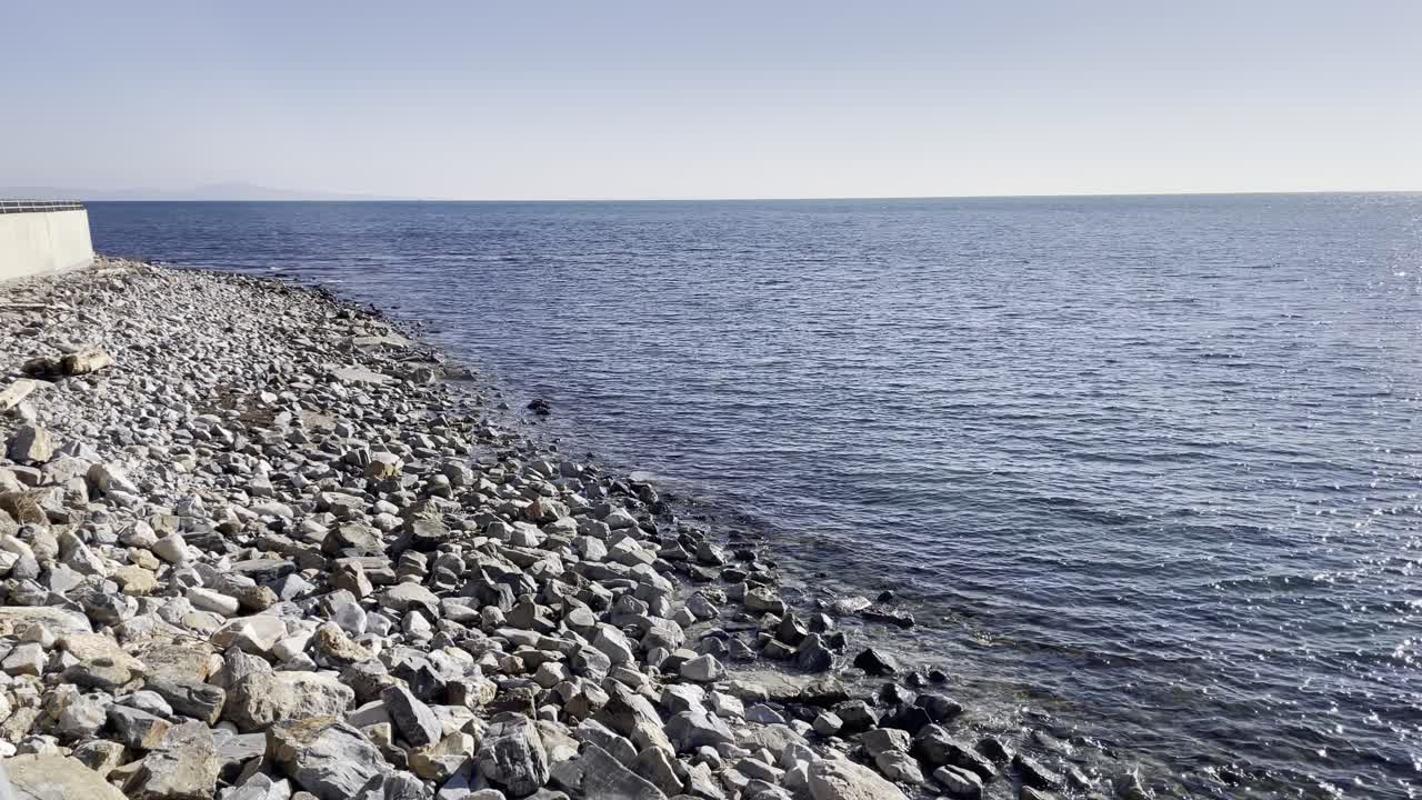 Scenic view of a rocky coastline meeting the calm blue sea under a clear sky, perfect for nature, travel, and coastal landscape themes