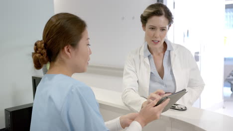 focused diverse female doctors using tablet and discussing over hospital reception desk, slow motion