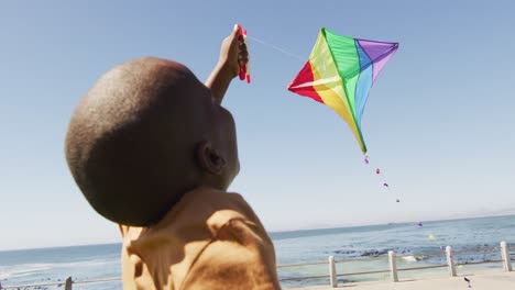 video of happy african american boy having fun with kite, running on beach