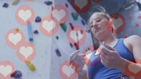 múltiples iconos de corazón flotando contra la mujer en forma caucásica aplicando tiza a sus manos en el gimnasio