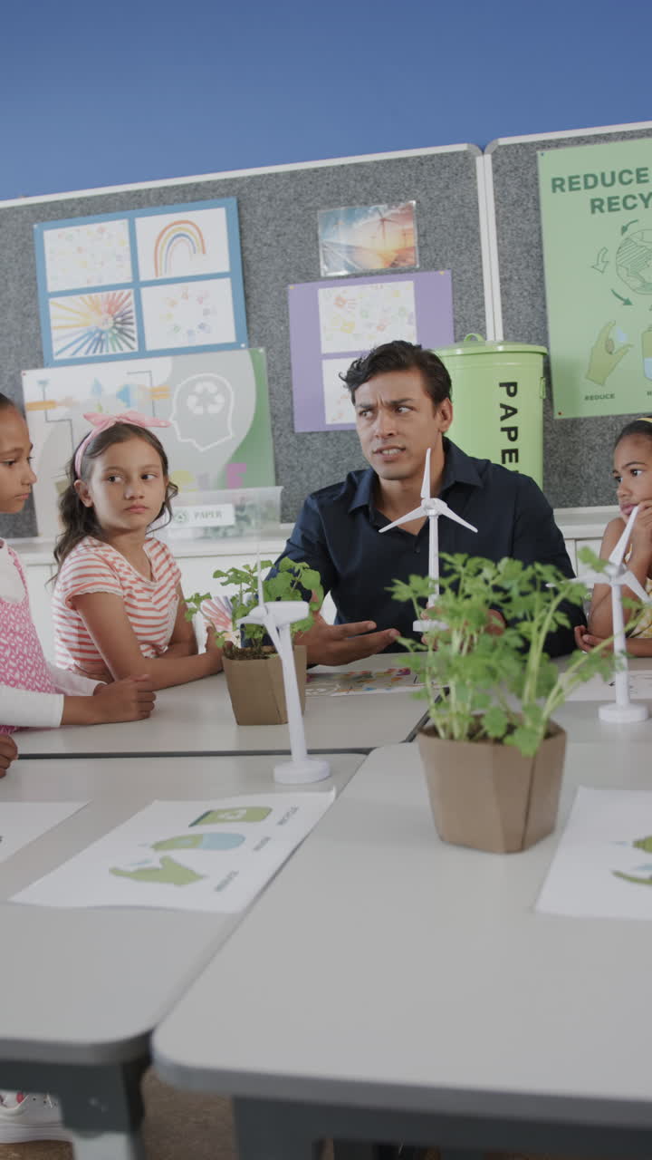 Vertical video of happy diverse male teacher and schoolchildren with ecology models in slow motion