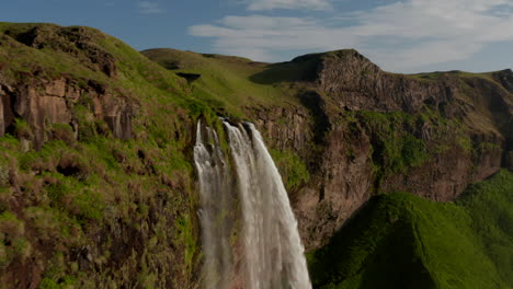 Vogelperspektive,-Die-über-Den-Atemberaubenden-Seljalandsfoss-Wasserfall-An-Der-Südküste-Islands-Fliegt.-Erstaunliche-Drohnenansicht,-Die-Eine-Moosige-Steinklippe-Und-Eine-Wasserkaskade-Im-Hochland-Zeigt