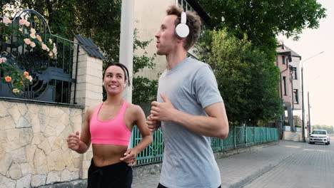 Beautiful-Runner-Girl-Wearing-Airpods-And-Sportive-Young-Man-With-Headphones-Running-Together-In-The-City-1