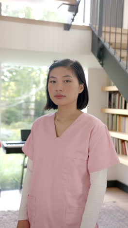 vertical video: physiotherapist in pink scrubs standing in modern home, looking at camera