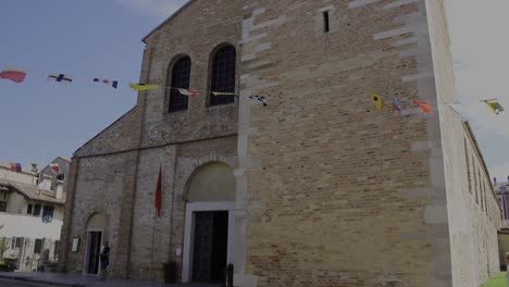 outside of a beautiful church with an italian flag. basilica of santa eufemia. minor basilica in grado, friuli-venezia giulia, italy, formerly a cathedral