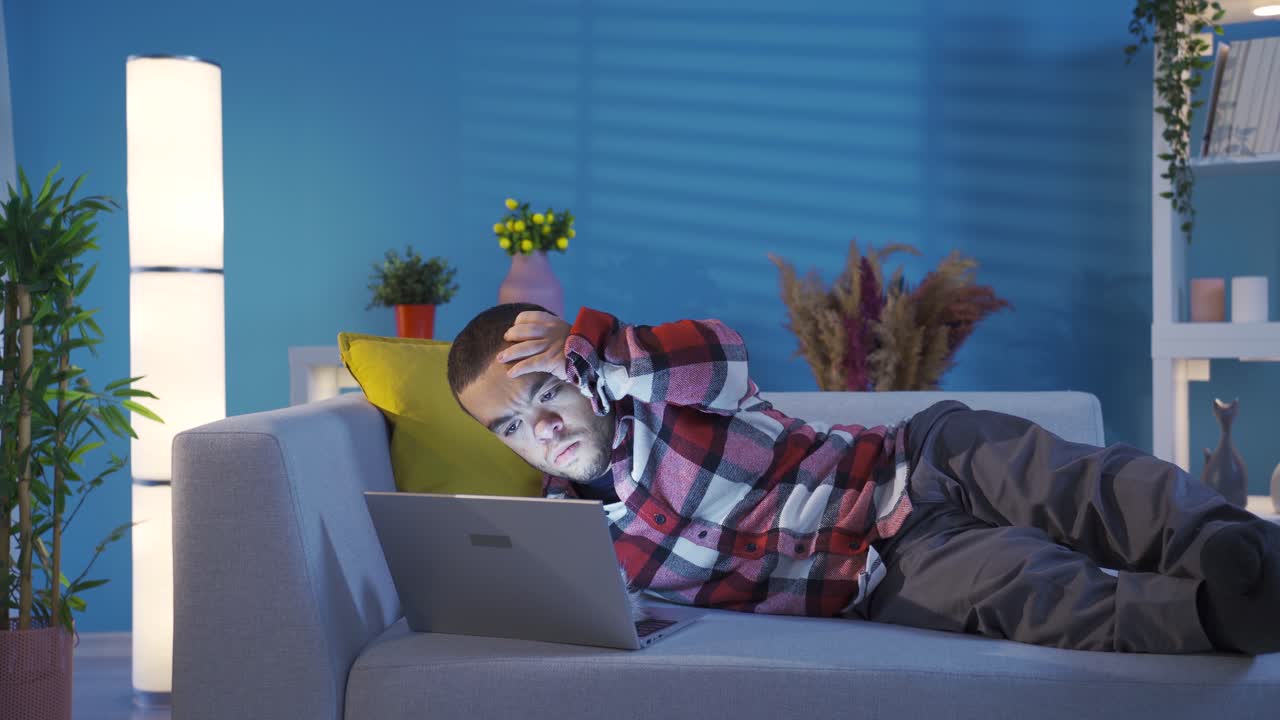 Kreativ og smart funksjonshemmet ung mann ligger på sofaen hjemme og skriver inn nye ideer på laptopen sin.