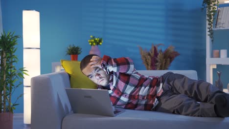creative and clever disabled young man lying on sofa at home and typing in new ideas using laptop.