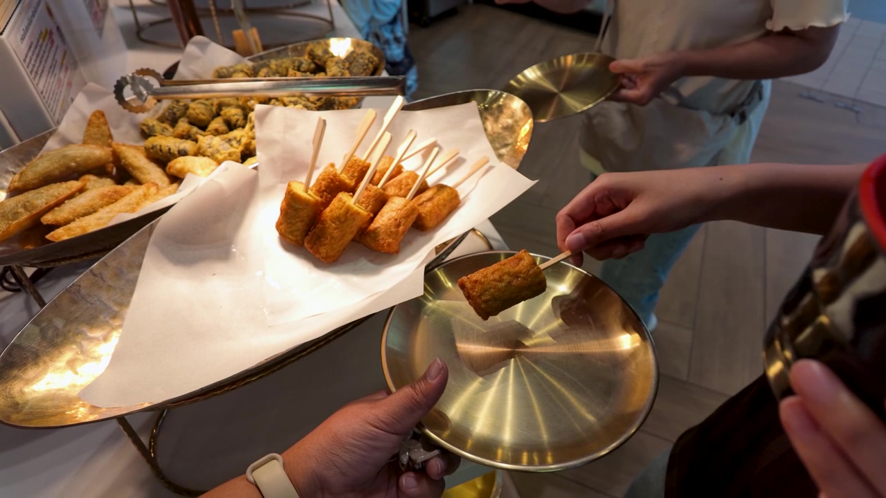 Persone che scelgono spiedini di tortini di pesce fritti a un buffet.