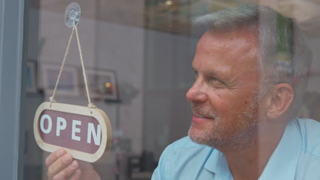 mature male owner or staff inside shop or cafe turning round sign from closed to open