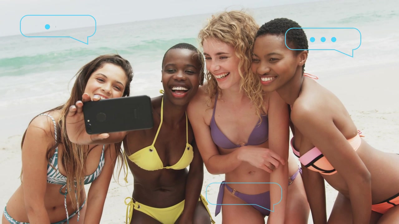 Quattro donne che allungano il telefono, in posa sulla riva, che si preparano per un selfie sociale mentre bolle di chat fluttuano.