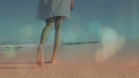 animación de la luz de la lente sobre la sección baja de la mujer joven biracial caminando descalza en la playa de arena.