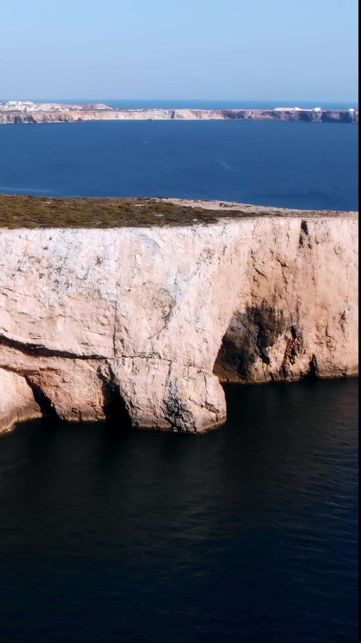 Scogliera calcarea aerea che si erge sul mare, parete rocciosa pallida a picco con grotte scavate e strati visibili