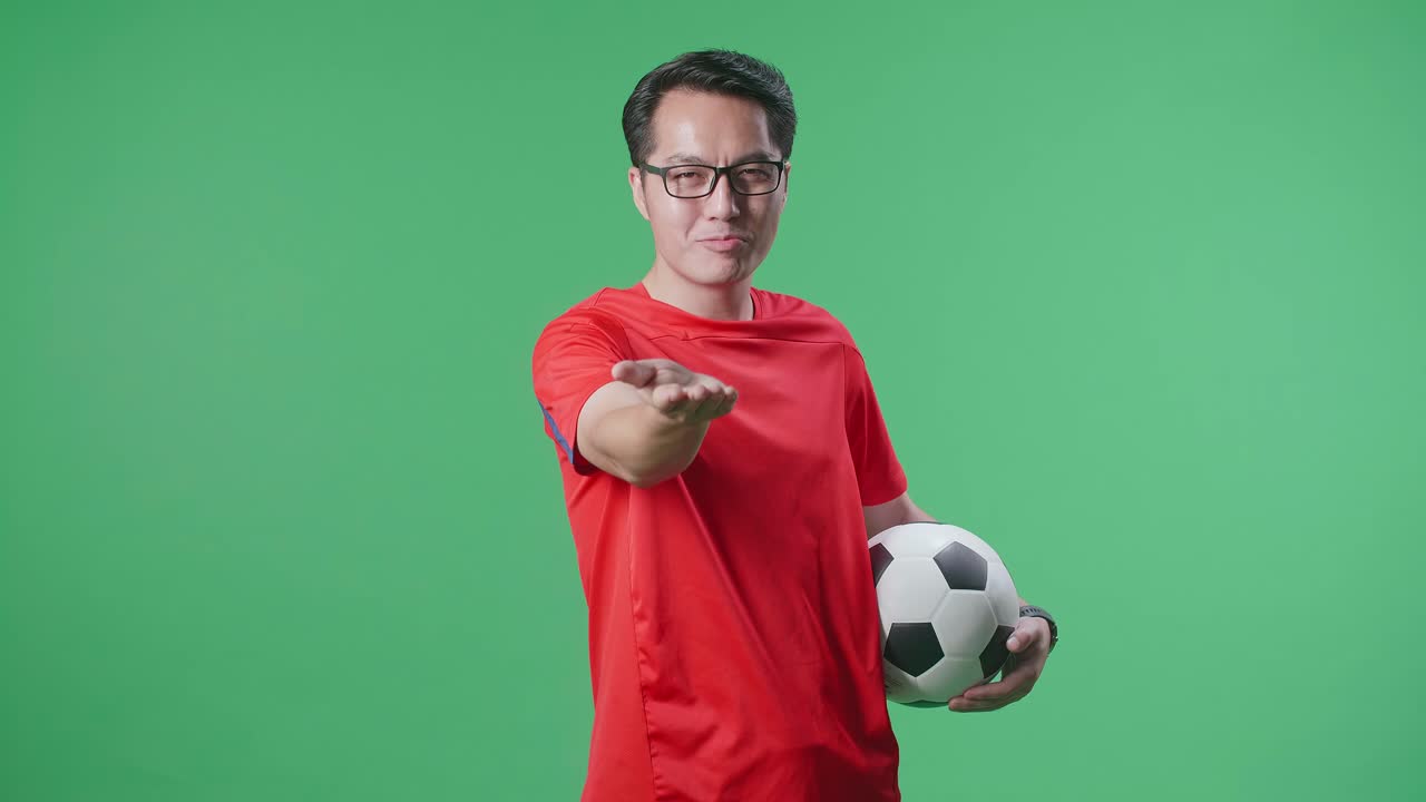 공을 고 카메라를 향해 미소 짓고 녹색 스크린 배경에서 축구를 응원하는 아시아인