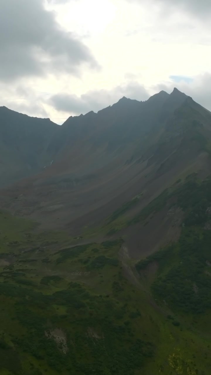 Rekaman udara yang menyapu pegunungan Vachkazhets di Krai Kamchatka, Rusia, memperlihatkan lereng vulkanik hijau, puncak berbatu yang tajam, dan lembah tundra di bawah langit mendung yang kelabu