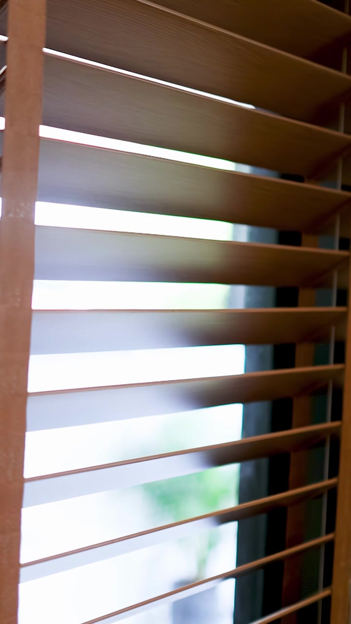 Close-up shot of wooden window shutters opening to let in bright natural daylight indoors