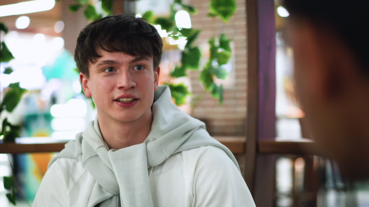 White guy looking steadily at friend while giving questioning expression, closeup showing raised eyebrow and slight lean, indoor casual conversation mood with subtle tension and curiosity in gaze