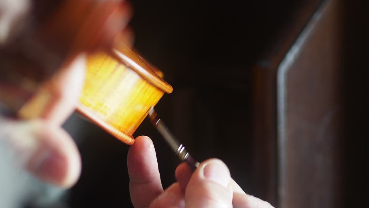 바이올린 제작자 루티에의 손이 손으로 만든 목조 현악기를 바르닝하고 있습니다.